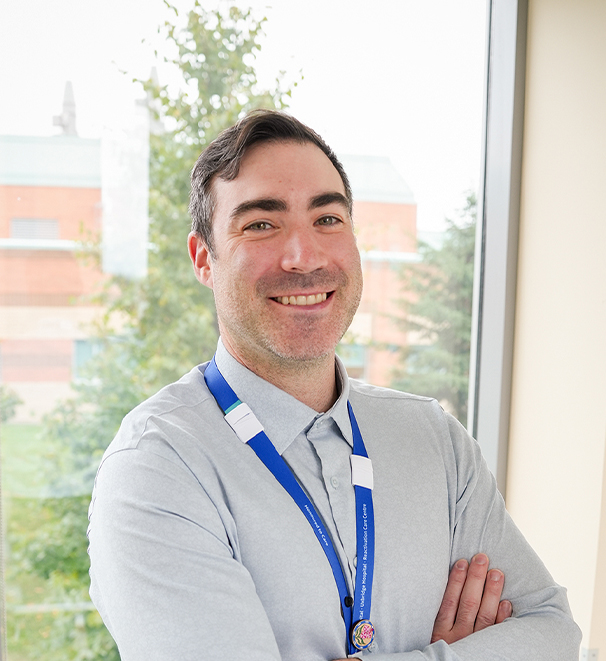 Staff stands smiling with arms crossed with window in background