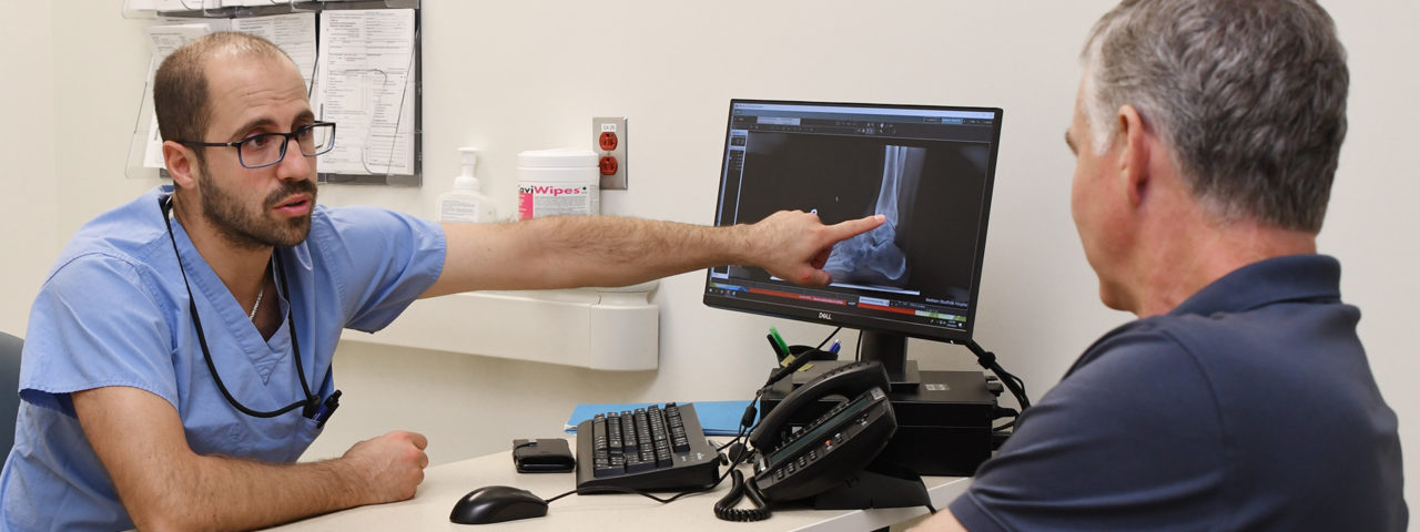a man points to an x-ray on a monitor and explains something to a patient