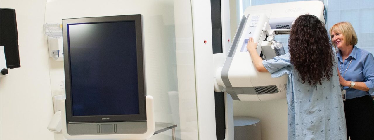 a patient stands at a mammogram machine while a doctor stands next to her