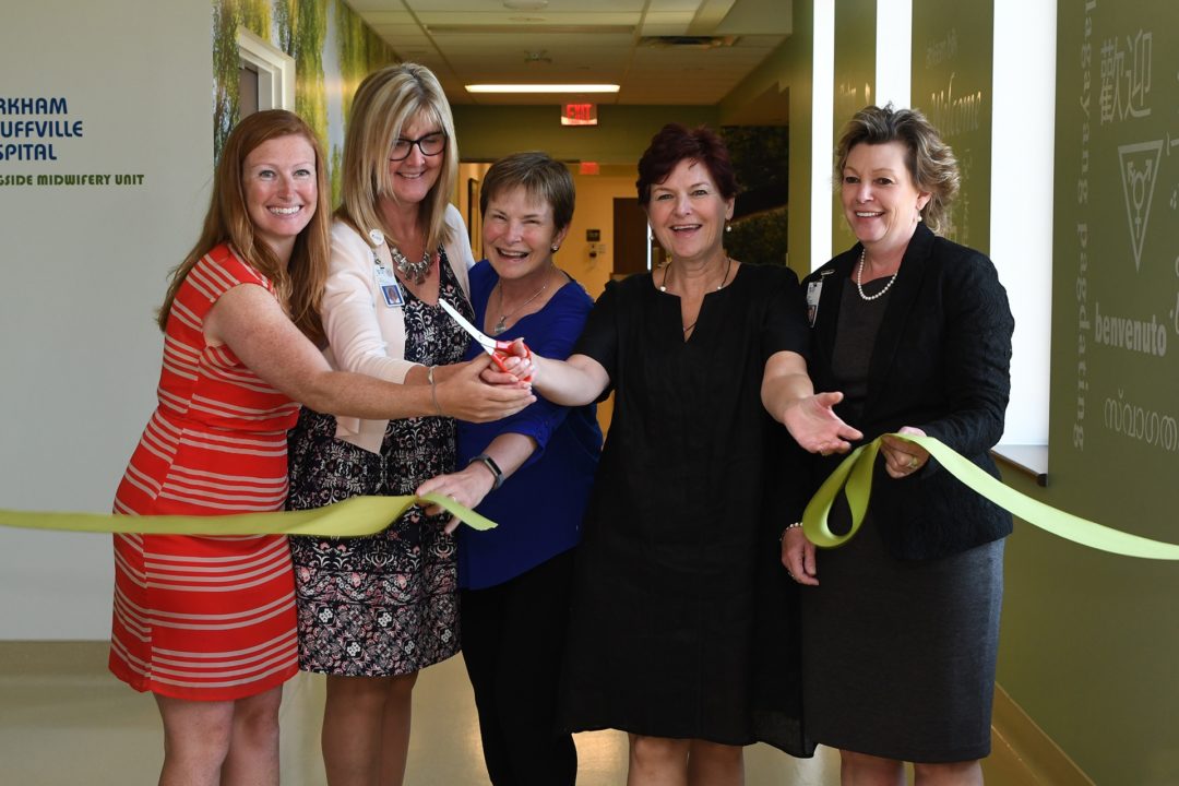several women stand together and cut a yellow ribbon, all are smiling