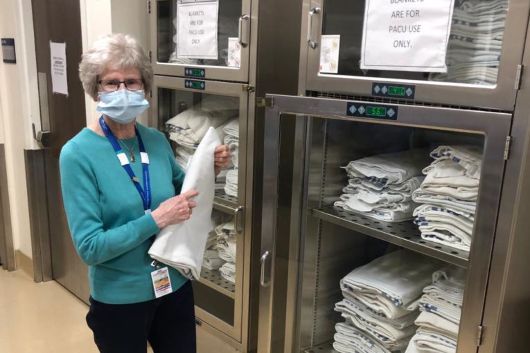 Carol, a volunteer, standing in front of towel warmers at the hospital