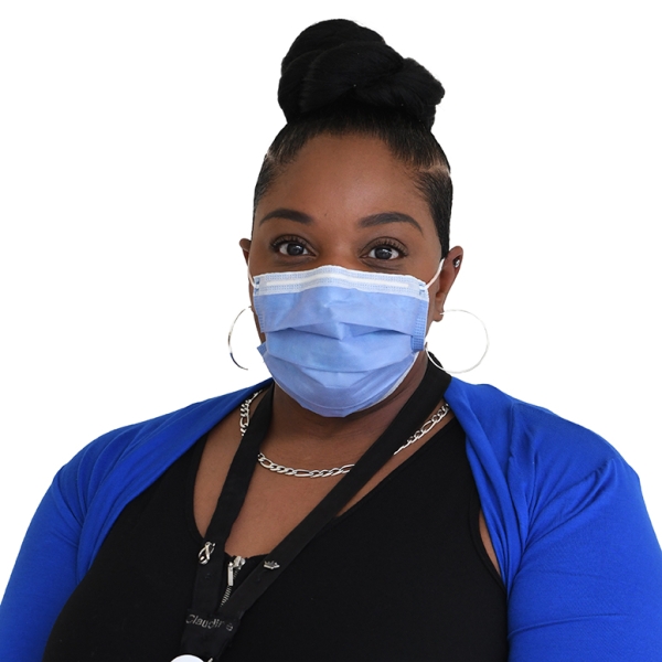 Claudine McDonald, seen from the chest up, wearing a blue cardigan, medical mask, and hair bun