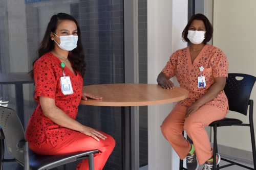 Rajdai and Nikki, both wearing scrubs, sit together at a wood table