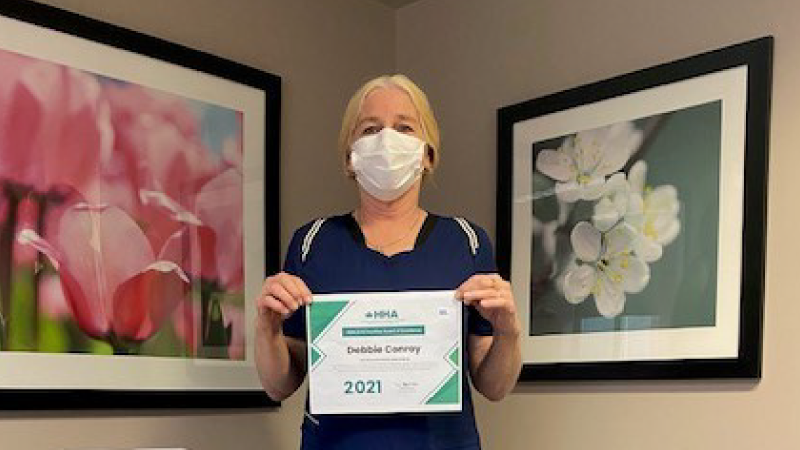 Debbie Conroy, wearing a medical mask, holding up her award of excellence