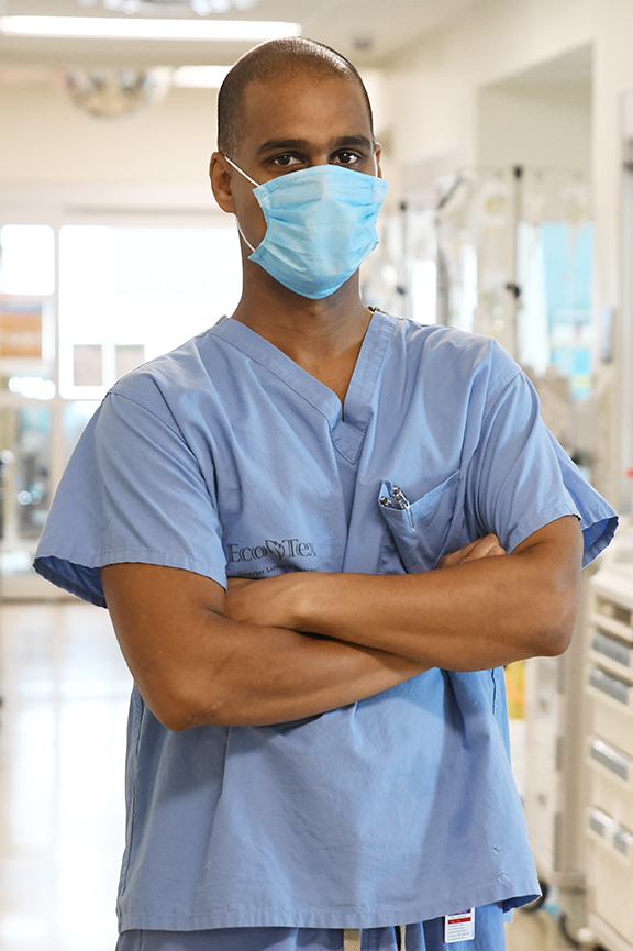 Dr. Doobay, seen from the waist up, wearing scrubs and medical mask, arms crossed