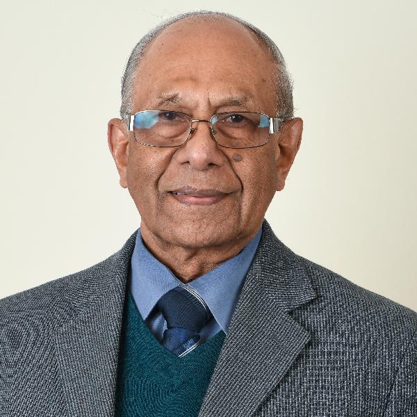 Dr. Emmanuel Persad seen from the chest up, wearing a grey suit and tie, glasses, and smiling