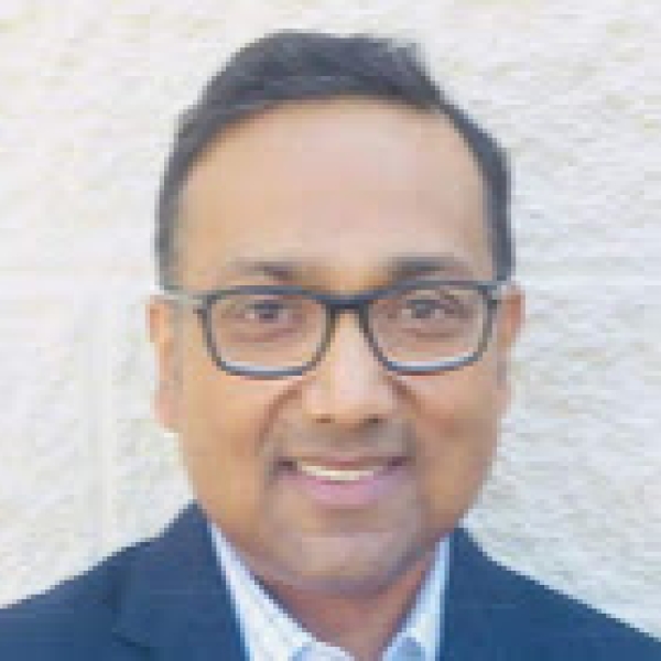 Faham Rashid from the shoulders up, wearing a blue suit jacket, glasses, and smiling