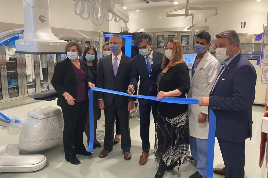 several people in suite stand in the new radiology suite and cut a blue ribbon