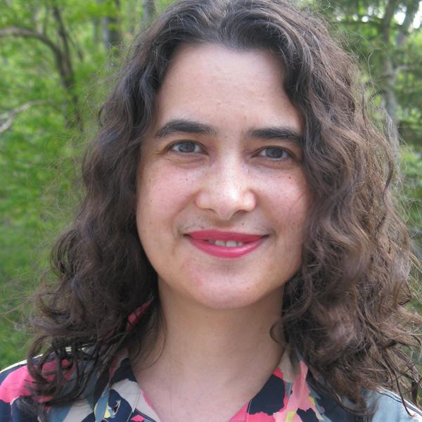 Dr. Gupta, wearing a floral shirt, pink lipstick, and shoulder length brown curly hair, smiling