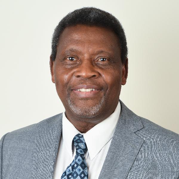 Dr. L. Kola Oyewumi seen from the chest up, wearing a grey suit and tie with short black hair, smiling