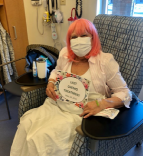 Lesley sitting in a hospital chair, holding a sign that says '"last chemo treatment"