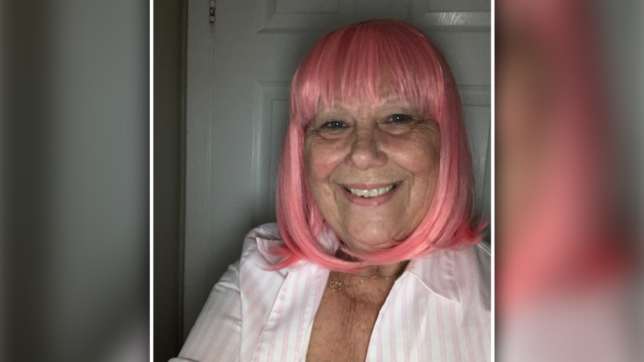 Lesley Web, wearing a pink wig and white button up shirt, smiling