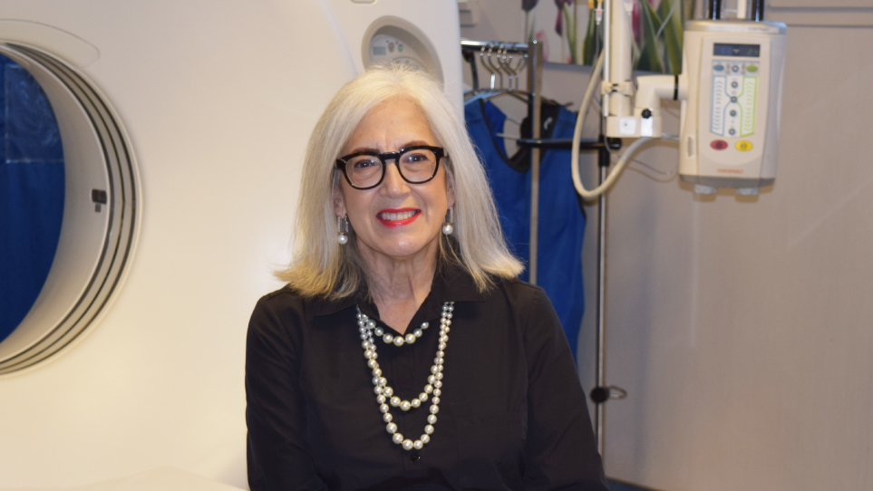 Lina Bigioni, wearing a black collared shirt, pearl necklace and earings, glasses, and shoulder length white hair