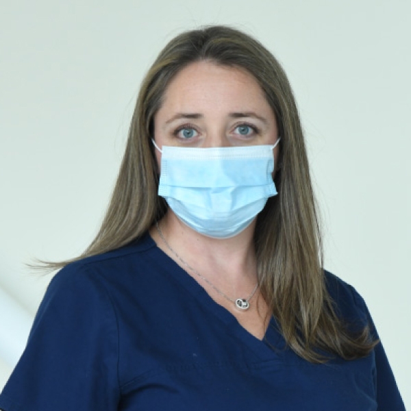 Natalie Létourneau seen from the chest up, wearing navy blue scrubs, medical mask, and shoulder length brown hair