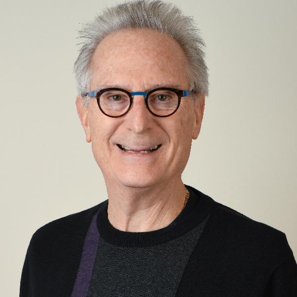 Dr. Neil Applebaum, seen from the chest up, wearing a black sweater, glasses, and short grey hair, smiling