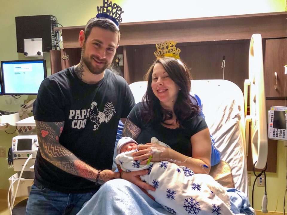 a new mother and father, wearing happy new year headbands, holding their newborn in a hospital bed