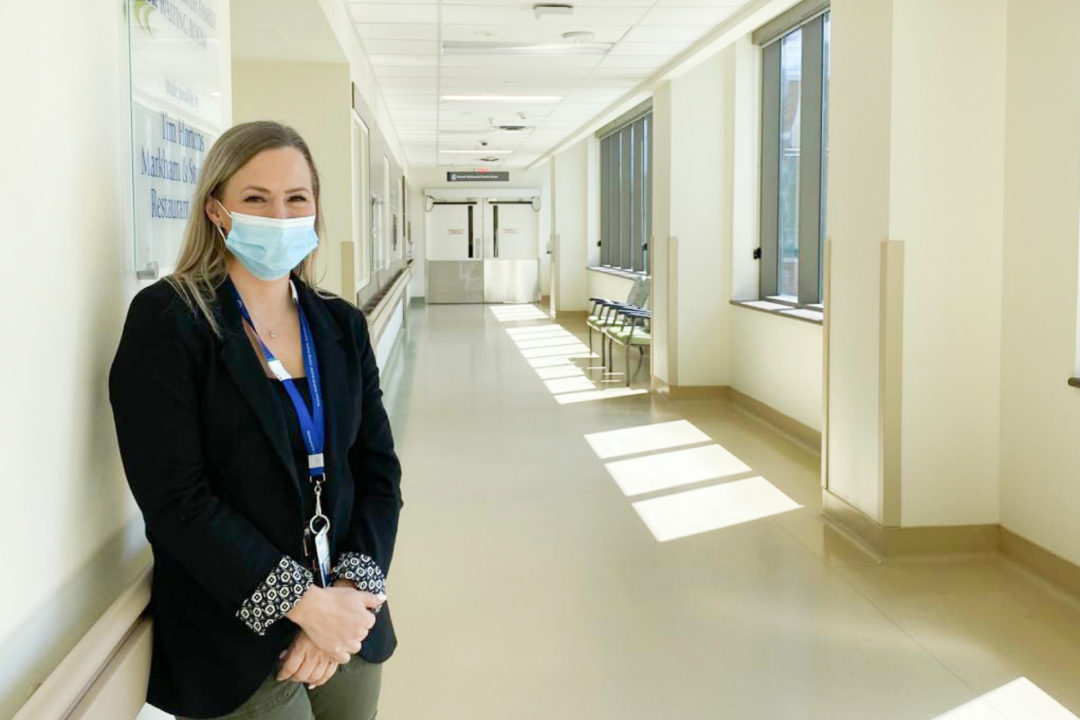 Pam Ingley, wearing business clothes and a medical mask, standing in a hospital hallway