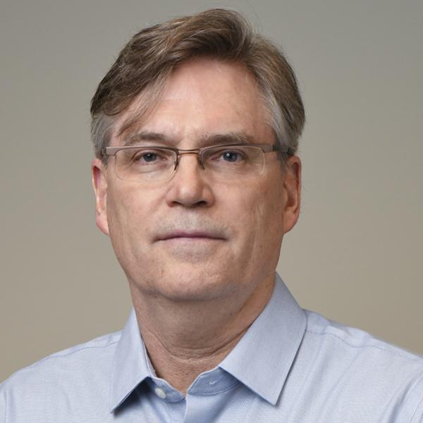 Dr. Peter Haw, seen from the shoulders up, wearing a blue collared shirt, glasses, and short brown hair