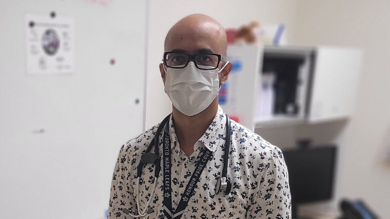 Dr. Raza Naqvi, wearing a patterned shirt, stethoscope, medical mask, and glasses