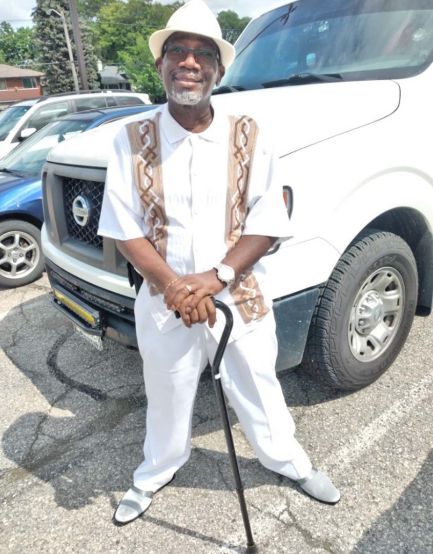 Roy Taylor, standing in front of a white truck, in an all white outfit, holding a cane