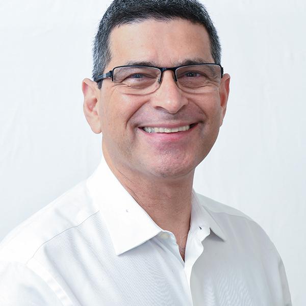 Dr. Rustom Sethna, seen from the chest up, wearing a white collared shirt and glasses, smiling