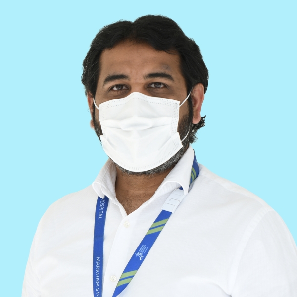 Saud Aslam, seen from the chest up, wearing a white collared shirt, medical mask, and short black hair