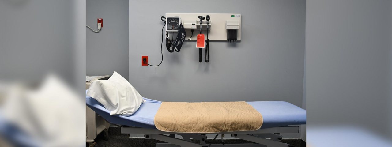 an examination bed, doctors equipment can be seeing hanging on the wall behind the bed