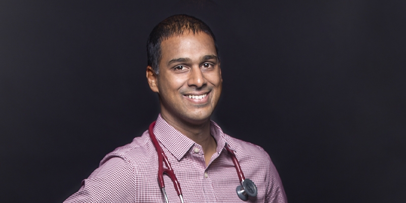 Dr. Anand Doobay, wearing a red collared shirt, stethoscope, and short black hair