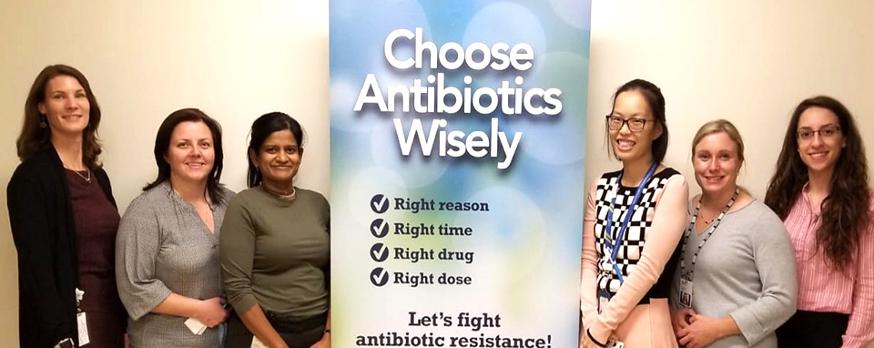 6 women stand together in front of a sign that says 'choose antibiotics wisely' and smile