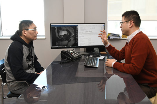 Frank Wang sits across the desk from his doctor while he points and explains something on his monitor