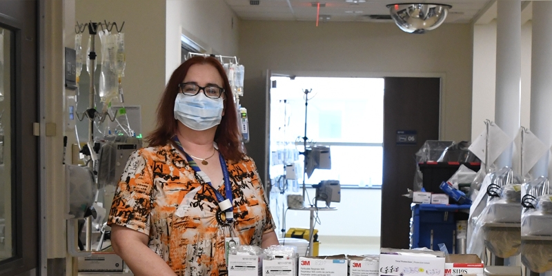 Christina Hazell, wearing orange scrubs, stands with a nursing cart in a hospital hallway