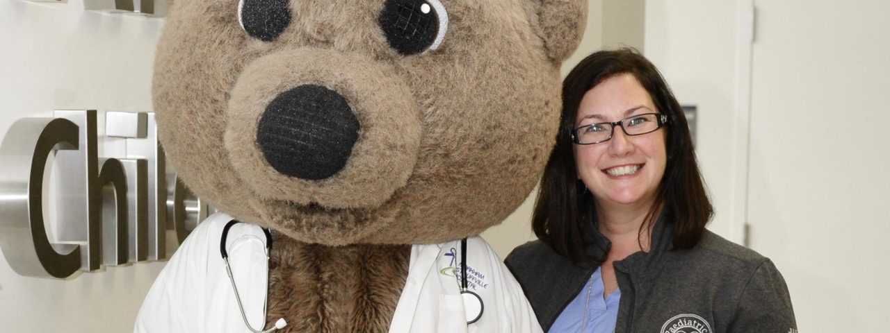 a woman stands next to Dr. Bear and smiles