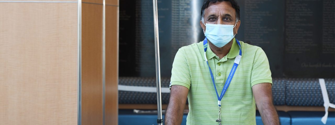 an elderly man wearing a green shirt and a medical mask poses for a photo