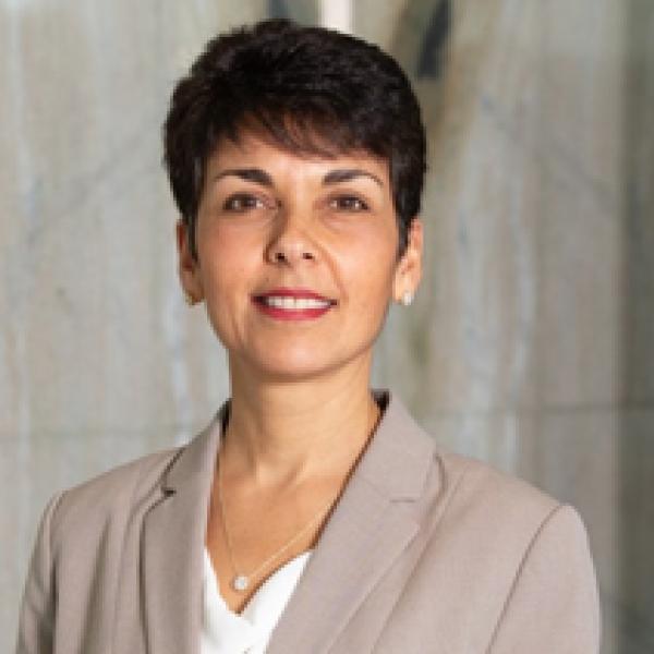 Marcia Mendes-d'Abreu from the shoulders up, wearing a brown suit jacket, short black hair, and smiling