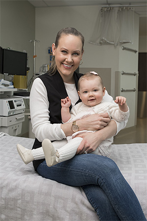 Megan Lewis sits on a hospital bed and holds her daughter, both are smiling