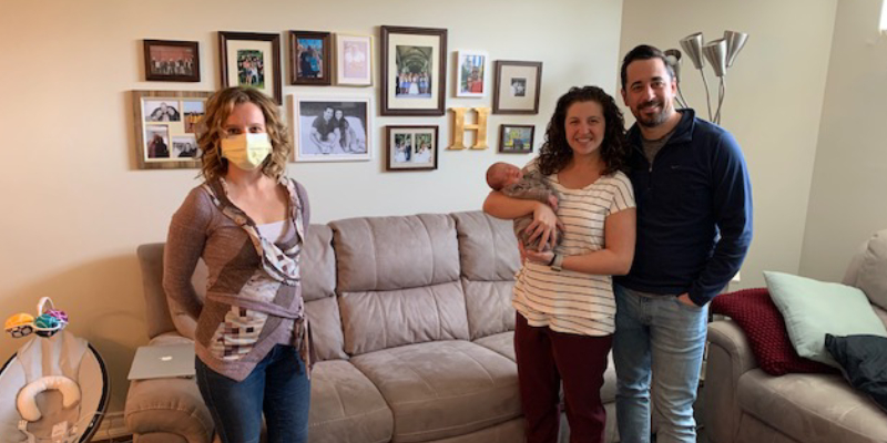 a new mother and father hold their newborn baby, while Stephanie Zaheer stands two feet away