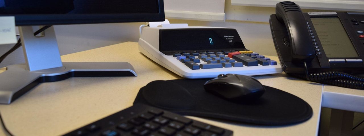 a desk with phone, monitor, mouse, and calculator