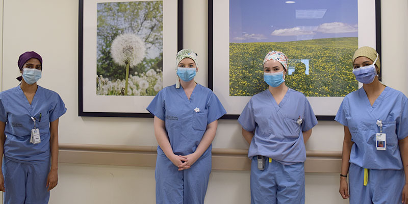 4 nurses in blue scrubs and medical masks stand together for a photo
