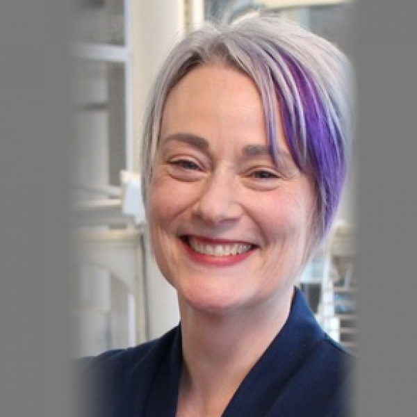 Susan Kennedy from the neck up, with short grey and purple hair, smiling
