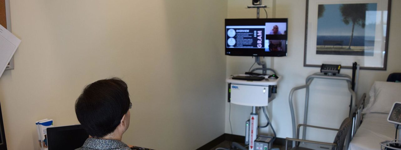 the head of a woman from behind is seen participating on a zoom call on a monitor in front of her