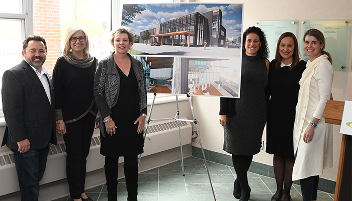 5 women and 1 man stand next to a photo of markham stouffville hospital on an easel and smile for the camera