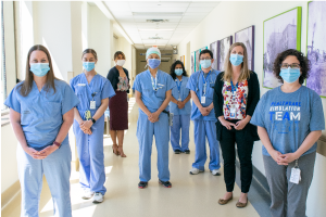 a group of doctors and nurses, all wearing scrubs and medical masks, stand together in a hospital hallway with hands clasped in front