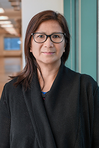 Rosemarie Ramirez, seen from the chest up, wearing a black cardigan, glasses, long brown hair, and smling