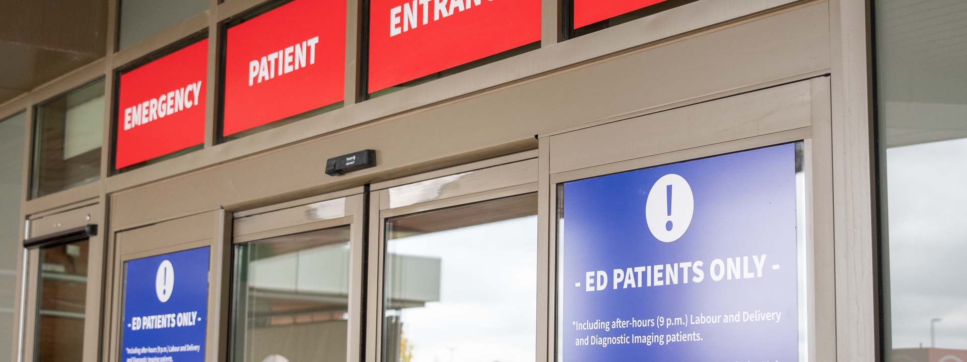 the emergency doors at markham stouffville hospital. a red sign can be seen with "emergency patient entrance" in white lettering