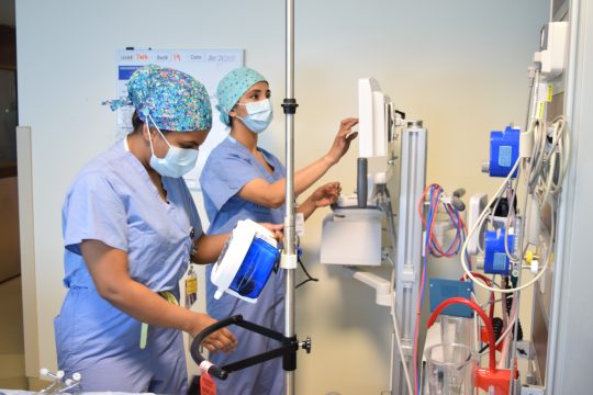 two nurses wearing masks adjust equipment inside the hospital.