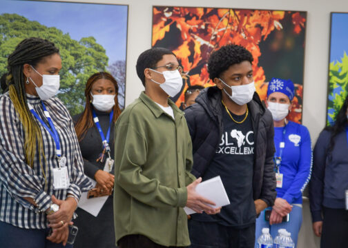 A crowd of six people wearing masks watching a presentation inside the hospital.