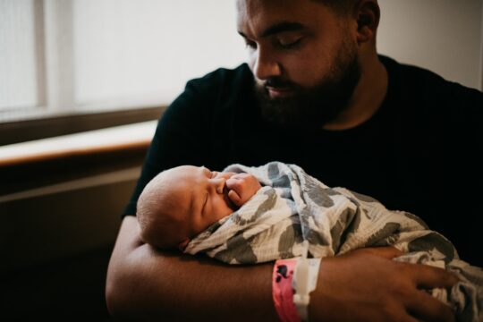 A man holds a baby wrapped in a blanket.