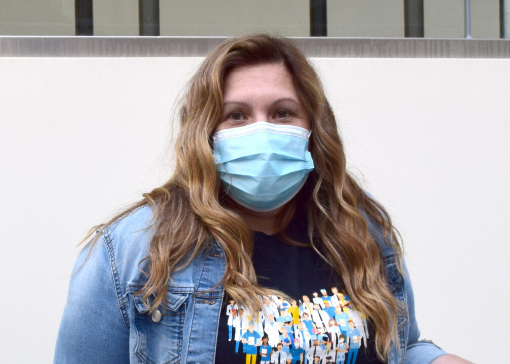 Amala standing in the hospital hallway wearing a blue mask and a blue shirt.
