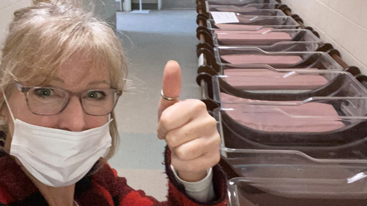Maggy Bell gives the thumbs up inside a hospital hallway with a row of bassinets lined up behind her.