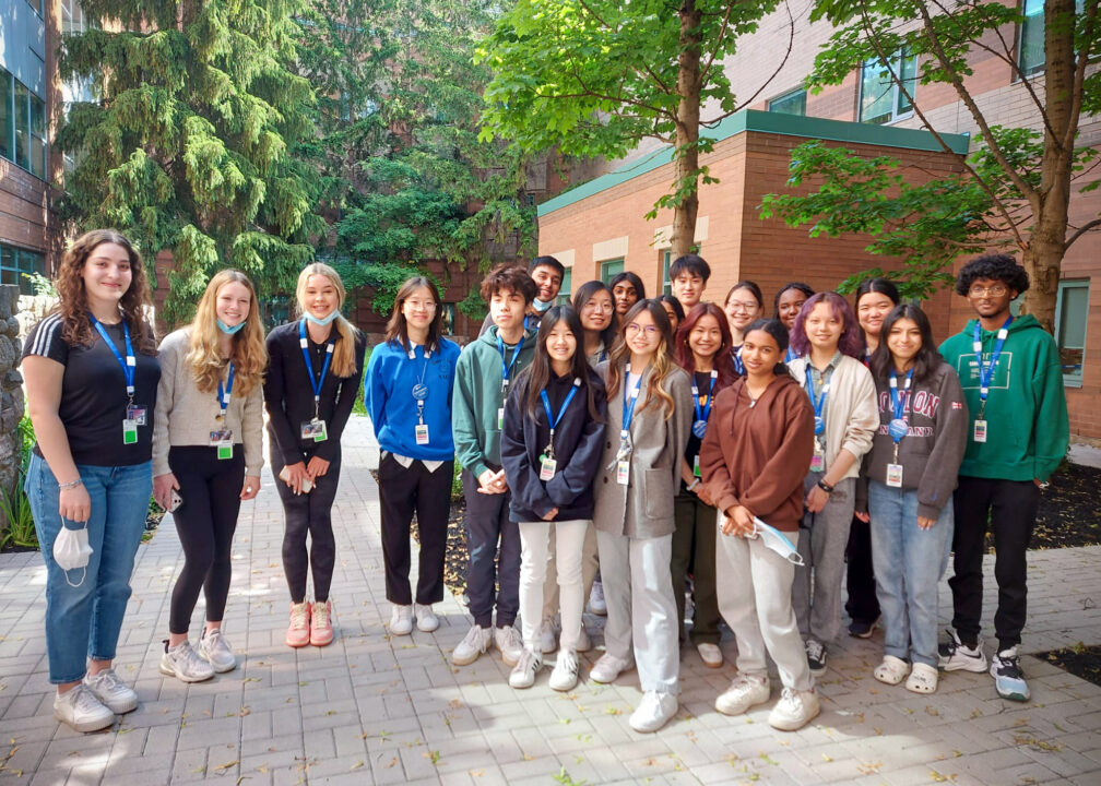 A group of high school students huddle together for a group photo outside in the wellness garden at Markham Stouffville Hospital.